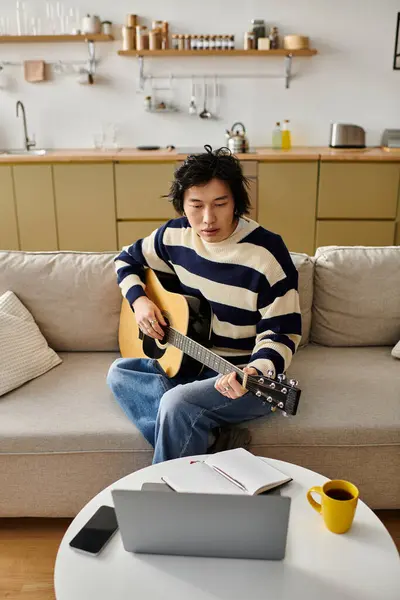 Un giovane concentrato si esercita a suonare la chitarra acustica seduto comodamente a casa. — Foto stock