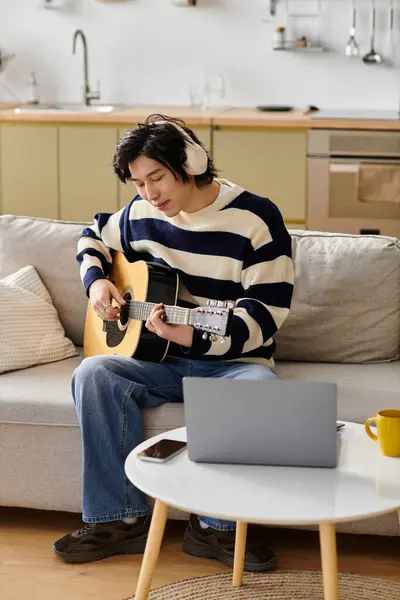 Handsome young man practices playing acoustic guitar while sitting comfortably on a couch. — Stock Photo
