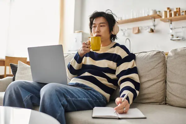 A young man immersed in online studies at home, enjoying a warm drink while taking notes. — Stock Photo