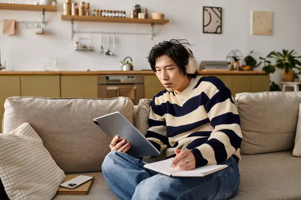 This young asian man is focused on his laptop, taking notes in a cozy home setting. — Stock Photo