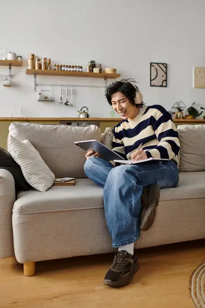 A handsome young student studies diligently at home, using his laptop and taking notes. — Stock Photo
