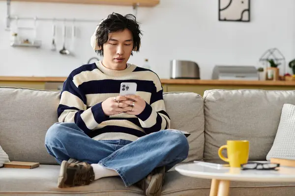 A stylish young Asian man lounges comfortably at home, engaged with his smartphone. — Stock Photo