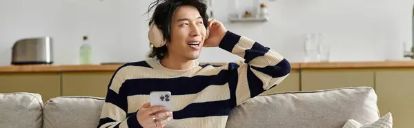 A handsome young man with headphones smiles while listening to music comfortably at home, banner — Stock Photo