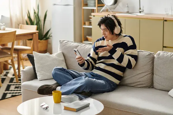 A handsome young man relaxes on a comfortable couch, engaged in a lively conversation on his phone. — Stock Photo