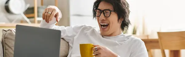 Jovem com óculos ri enquanto estuda on-line em casa, tomando café de uma caneca amarela, banner — Fotografia de Stock