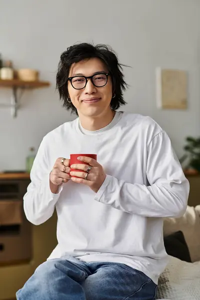 A good looking young man relaxes at home, sipping from a red cup in a stylish apartment. — Stock Photo