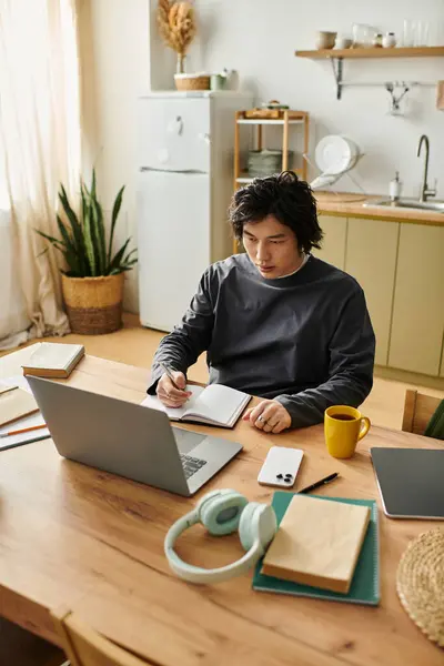 Focused student writes notes while studying on laptop at home during the day in cozy kitchen. — Stock Photo