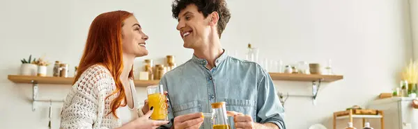 A young couple shares playful laughter in their cozy kitchen while enjoying refreshing drinks. — Stock Photo