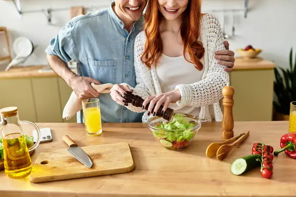 Young couple shares joyful moments in their cozy kitchen, crafting a healthy salad with care. — Stock Photo