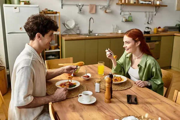 Young couple sits at a dining table, sharing a joyful meal and laughter in a cozy home. — Stock Photo
