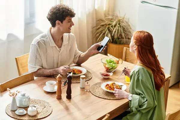 A young couple enjoys pasta and salads at home, laughing and savoring their time together. — Stock Photo