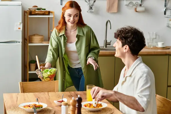 In a warm kitchen, a cheerful woman serves salad to her partner, spreading love and coziness. — Stock Photo