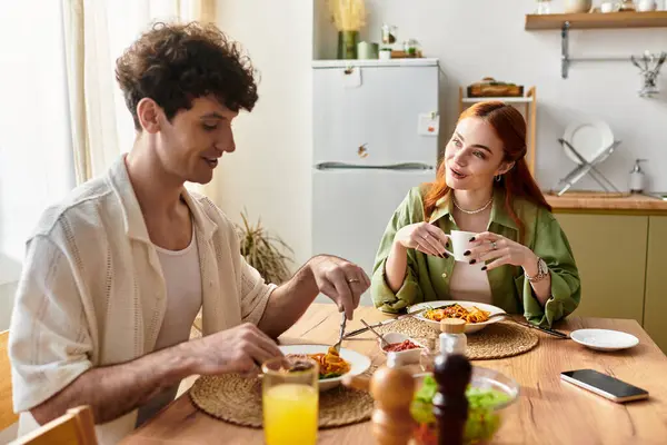 Una joven pareja comparte una deliciosa comida en casa, apreciando la compañía de los demás y riendo. - foto de stock