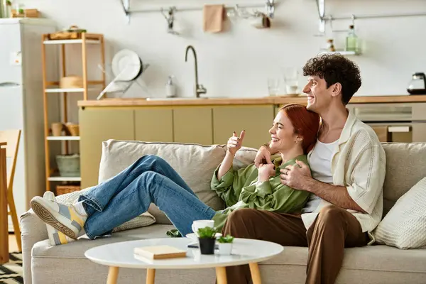 A young couple smiles and laughs together while lounging on their couch. — Stock Photo