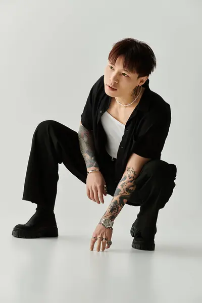 A stylish young Asian man crouches in a contemporary studio, exuding creativity and confidence. — Stock Photo