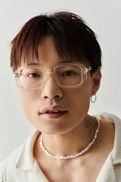 Young man showcases his trendy style with glasses and unique jewelry in a modern setting. — Stock Photo