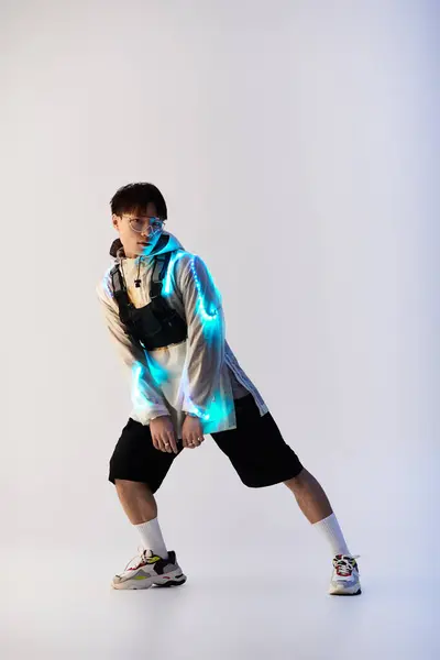 A young handsome Asian man strikes a dynamic pose in a stylish outfit, illuminated with blue lights. — Stock Photo