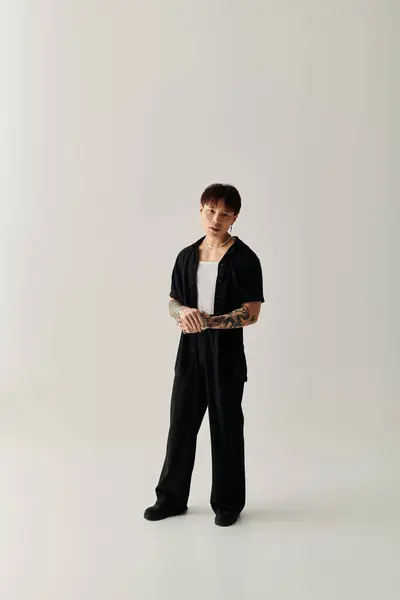 Un joven guapo asiático se levanta con confianza en un traje negro chic contra un simple telón de fondo. - foto de stock