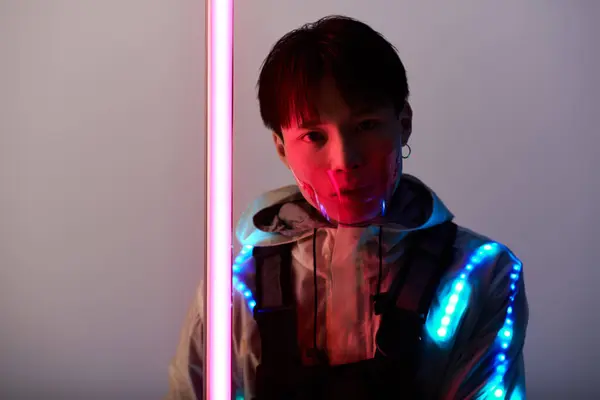 A stylish young Asian man in a futuristic outfit shines under neon lights. — Stock Photo