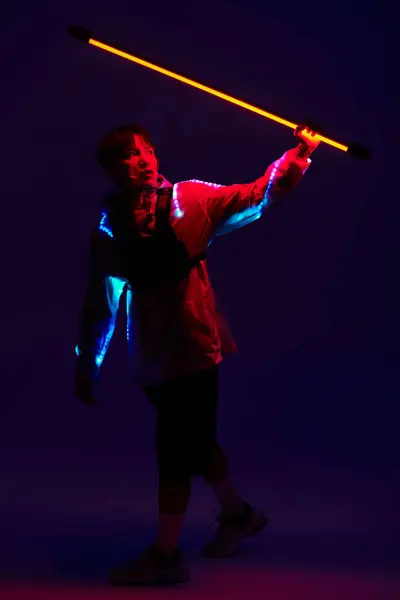 A stylish young Asian man wields a glowing stick amidst vibrant lights. — Stock Photo