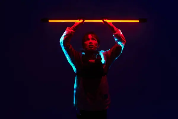 A confident young man holds a glowing neon bar above his head, showcasing his stylish attire. — Stock Photo
