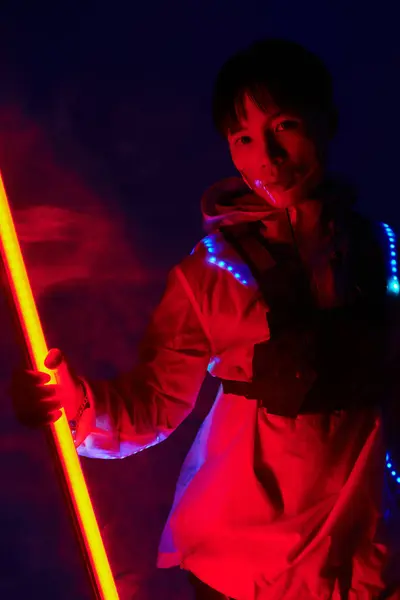 Ein junger gutaussehender asiatischer Mann präsentiert seinen stylischen Look, während er einen leuchtenden Lichtstab in der Hand hält. — Stockfoto