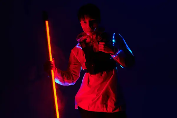 Ein junger asiatischer Mann zeigt sein stylisches Outfit mit einem leuchtenden Stock in einer lebendigen Umgebung. — Stockfoto