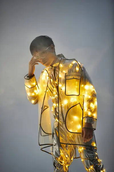 A young handsome Asian man stands confidently, wearing a reflective outfit covered in bright lights. — Stock Photo