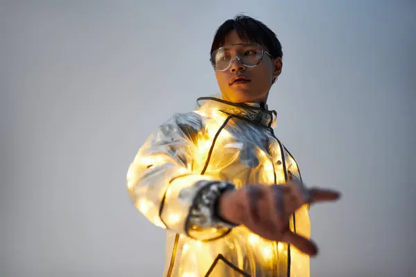 Young handsome man poses confidently outdoors, showcasing a trendy illuminated jacket at dusk. — Stock Photo