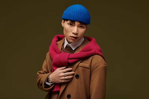 In a chic indoor space, a young man enhances his style with a blue beanie and red scarf. — Stock Photo