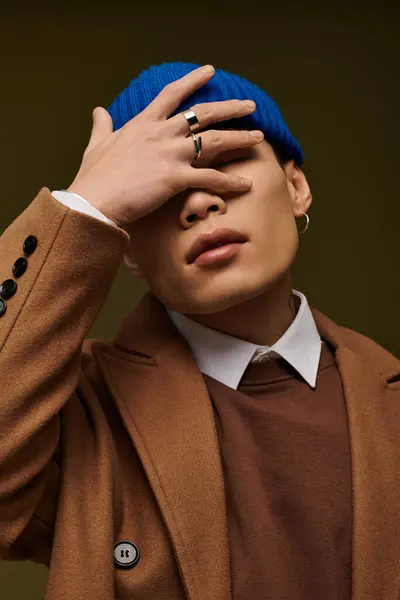 A stylish young Asian man poses confidently in a brown coat and bright blue beanie. — Stock Photo