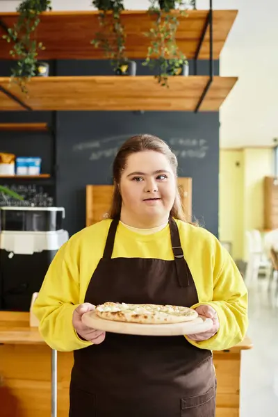 In a lively cafe, a young woman with Down syndrome proudly displays a fresh pizza. — Stock Photo