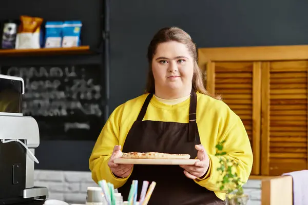Young woman with Down syndrome stands proudly in a cafe, holding freshly baked treats on a tray. — Stock Photo