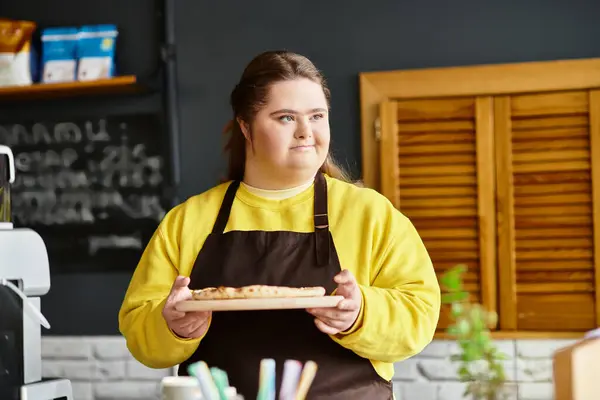 Strong young woman in casual attire holds a tray of cookies in a welcoming cafe atmosphere. — Stock Photo