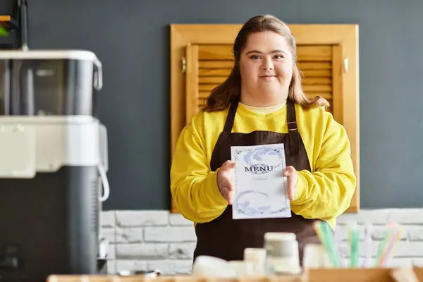 A young woman with Down syndrome proudly presents a menu in a warm cafe. — Stock Photo