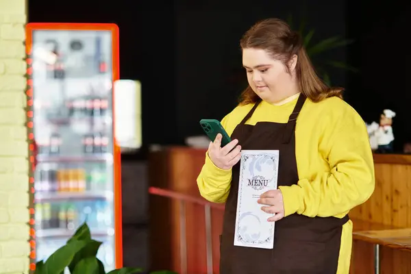 Young woman with Down syndrome stands confidently in the cafe, browsing the menu on her phone. — Stock Photo