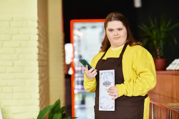 A confident young woman with Down syndrome stands holding a menu in a cozy cafe. — Stock Photo