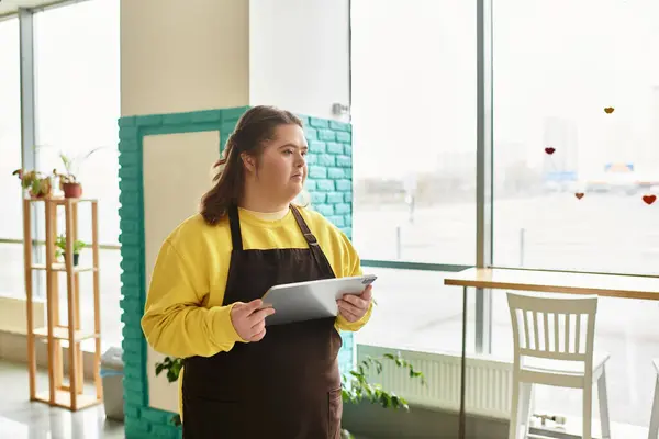 Una mujer joven con síndrome de Down está parada en un café, con confianza usando una tableta. — Stock Photo
