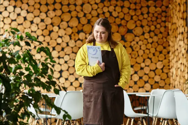 A young woman with Down syndrome stands proudly in a lively cafe, showcasing her spirit. — Stock Photo