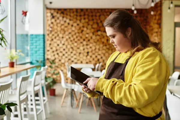 In a lively cafe, a young woman with Down syndrome engages with her tablet, radiating confidence. — Stock Photo