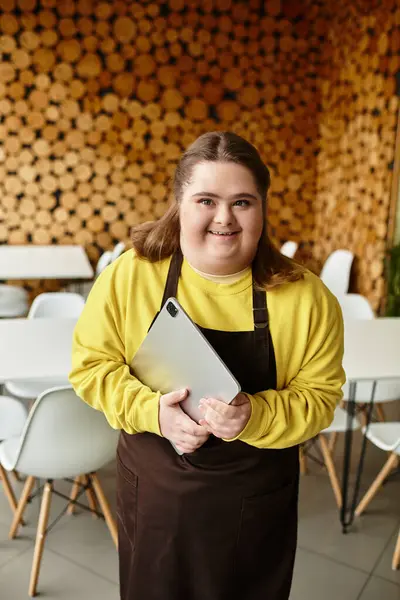 A young woman with Down syndrome smiles in a bright yellow sweater at a cozy cafe. — Stock Photo