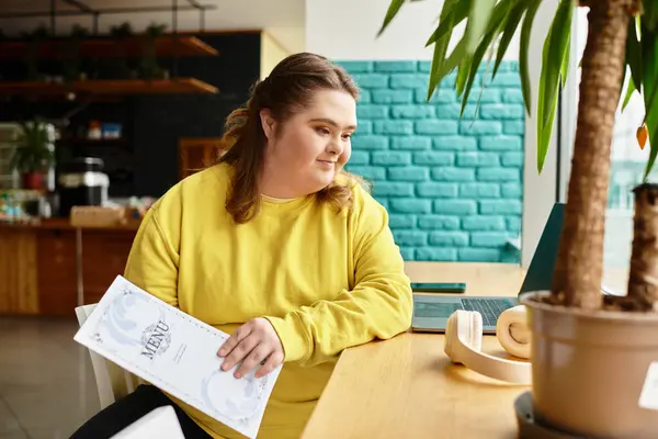A young woman with Down syndrome sits in a cafe, happily engaging with the menu. — Stock Photo