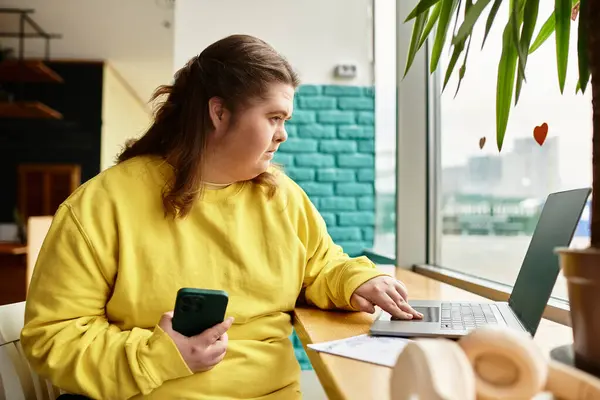 Brightly dressed young woman engages with her laptop in a warm and inviting cafe setting. — Stock Photo