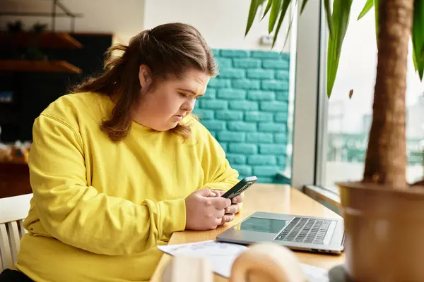 Young woman with Down syndrome relaxes at a cafe, focused on her smartphone and laptop. — Stock Photo