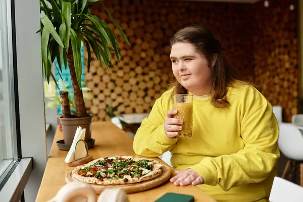 A confident young woman enjoys pizza and a drink in a cafe, showcasing her strong spirit. — Stock Photo