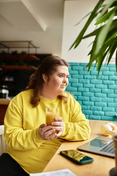 In a bright cafe, a young woman with Down syndrome confidently sips her drink while working. — Stock Photo