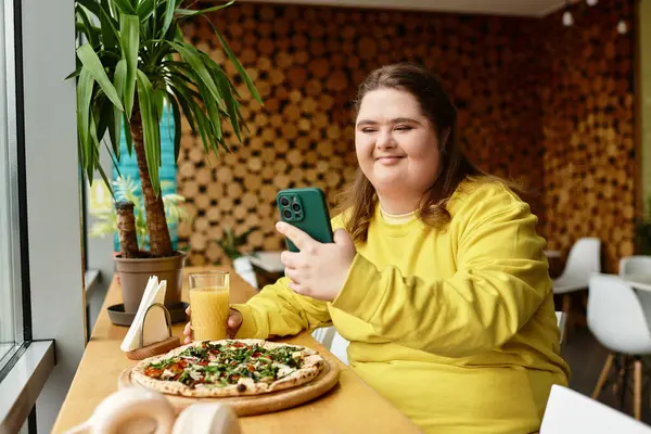 Una giovane donna con la sindrome di Down sorride ad un caffè, usando con fiducia il suo telefono tra decorazioni luminose. — Stock Photo