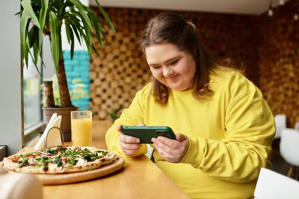 A young woman with Down syndrome smiles at her phone while savoring a delicious meal in a cafe. — Stock Photo