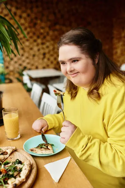 Junge Frau mit Down-Syndrom lächelt strahlend, während sie ihre Mahlzeit in einem warmen Café-Ambiente genießt. — Stockfoto