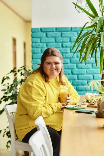 Brightly dressed young woman with Down syndrome relaxes in a lively cafe with a drink and food. — Stock Photo